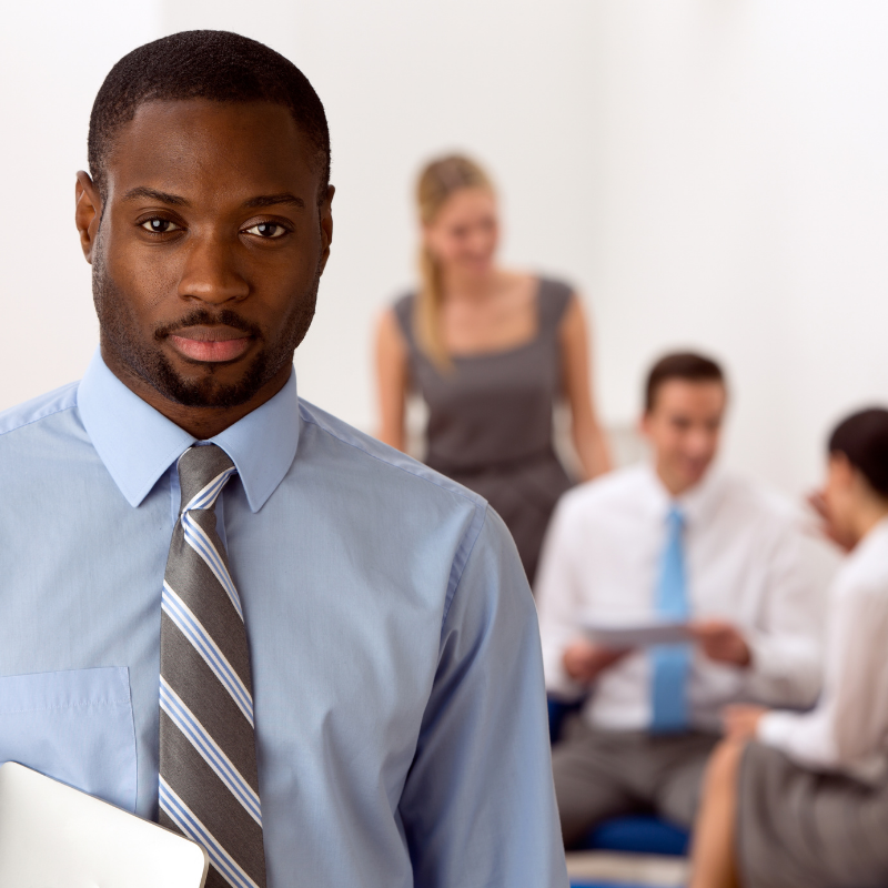 A lawyer stands in the foreground looking at the camera with three people in the background talking.