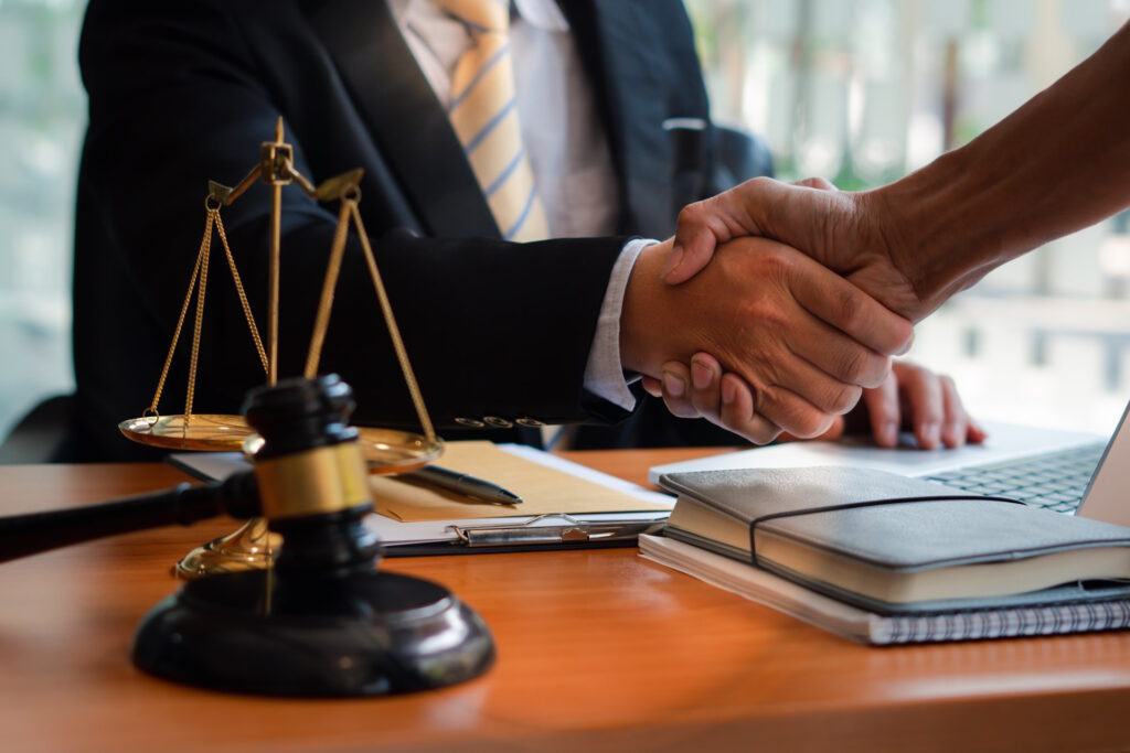 The image shows a lawyer shakes hands with another person across a desk. A gavel sits on the desk