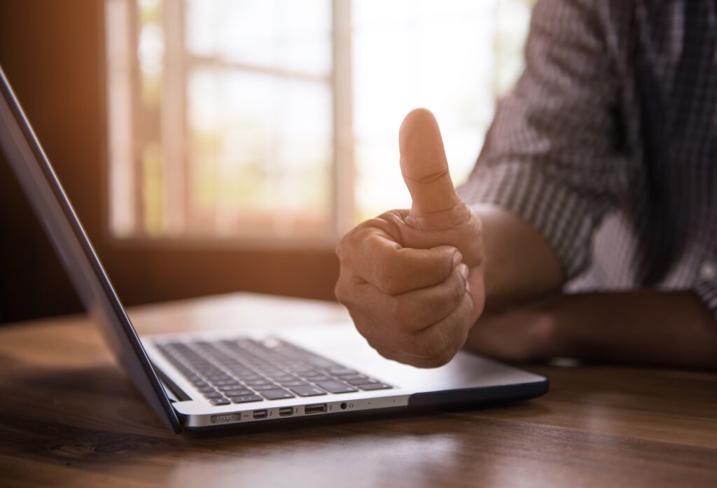 A businessman giving a thumbs up at his laptop.