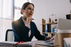 female lawyer in eyeglasses at workplace with documents and laptop in office