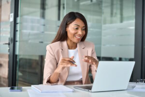 Happy professional young business woman hr manager team leader executive wearing suit working in office looking at laptop having video conference call virtual online meeting.