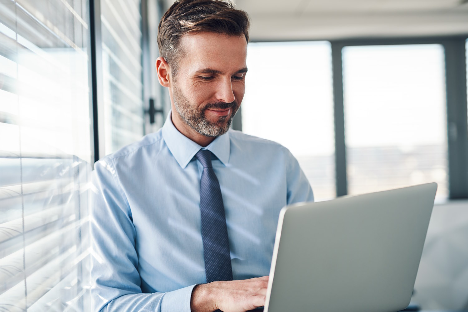 Businessman in modern office typing on a laptop sitting on his desk