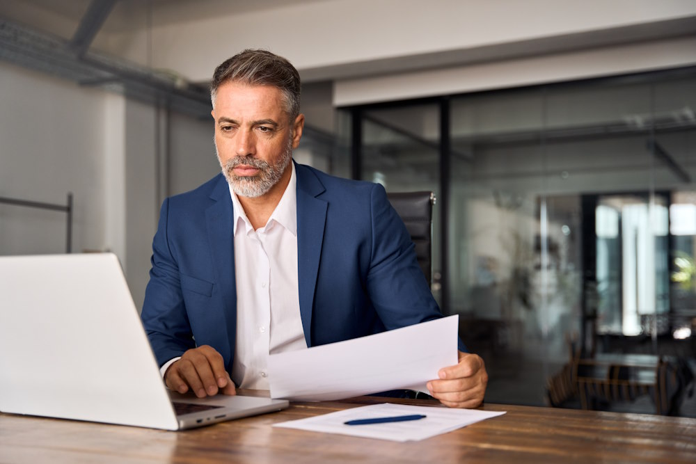 Middle-age man sitting at a desk using a laptop in a modern office.